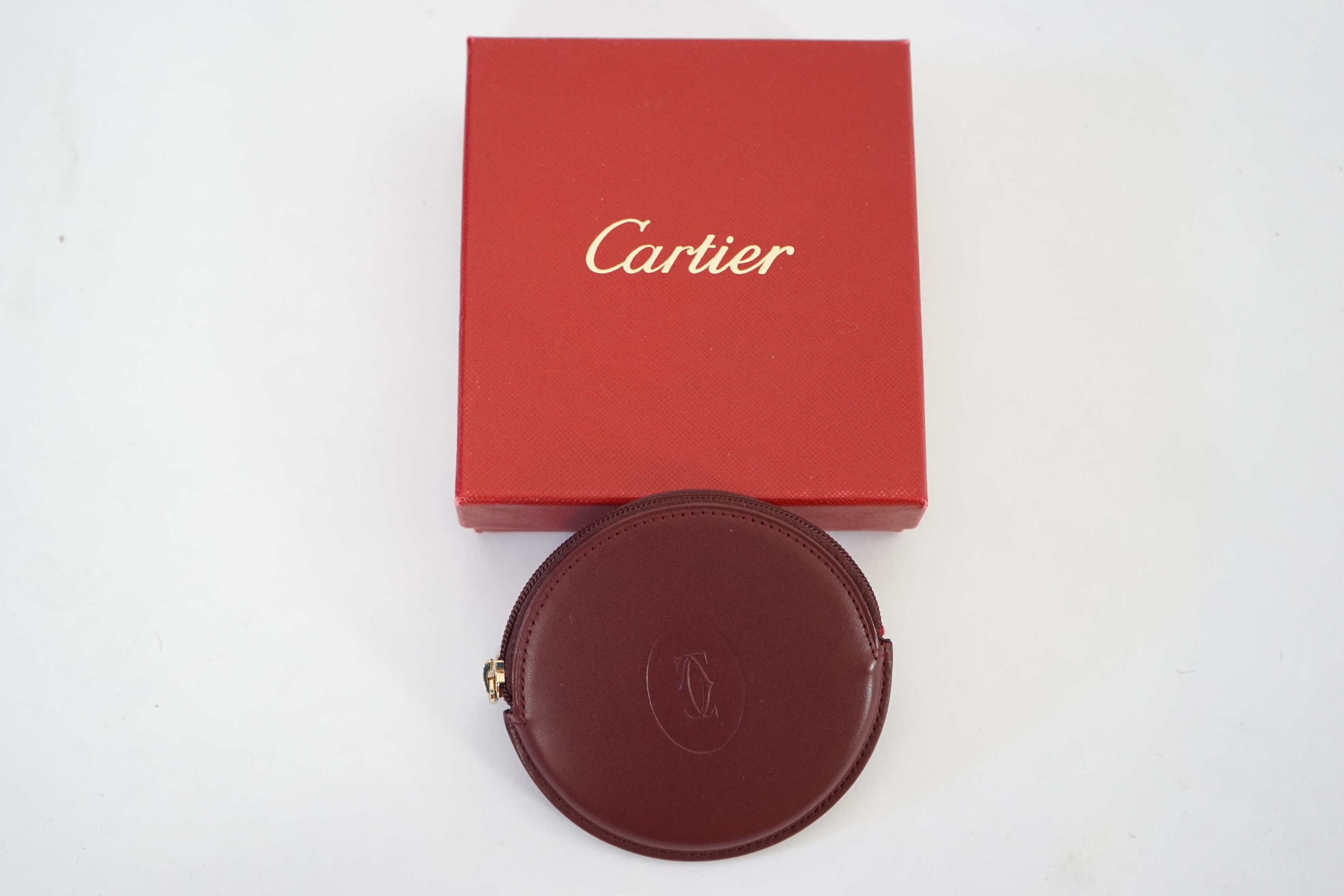 A Cartier maroon leather circular purse with box.